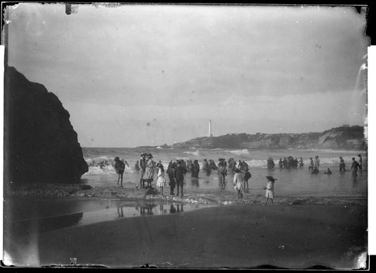 La grande plage de Biarritz à la fin du XIXe siècle : baigneurs dans les vagues, le phare de la pointe Saint-Martin au loin.